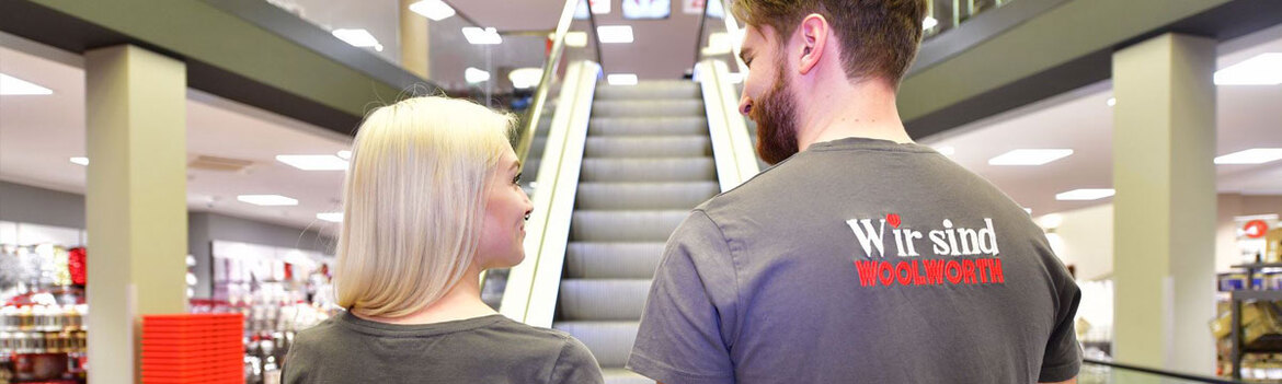 Junge Frau und junger Mann stehen vor Rolltreppe in Kaufhaus